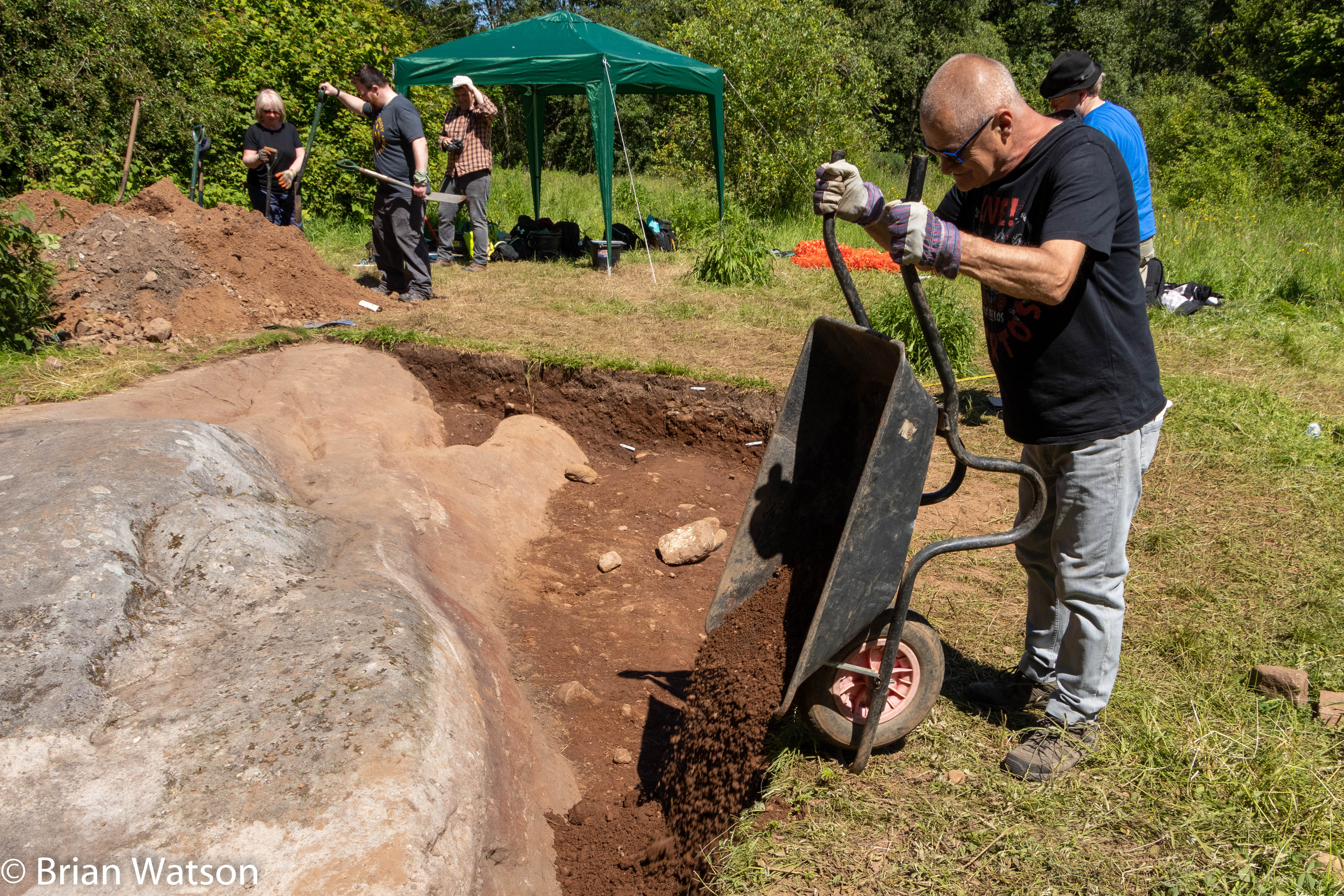 Tipping soil from a wheelbarrow into the trench at the Faifley Rocks excavation.