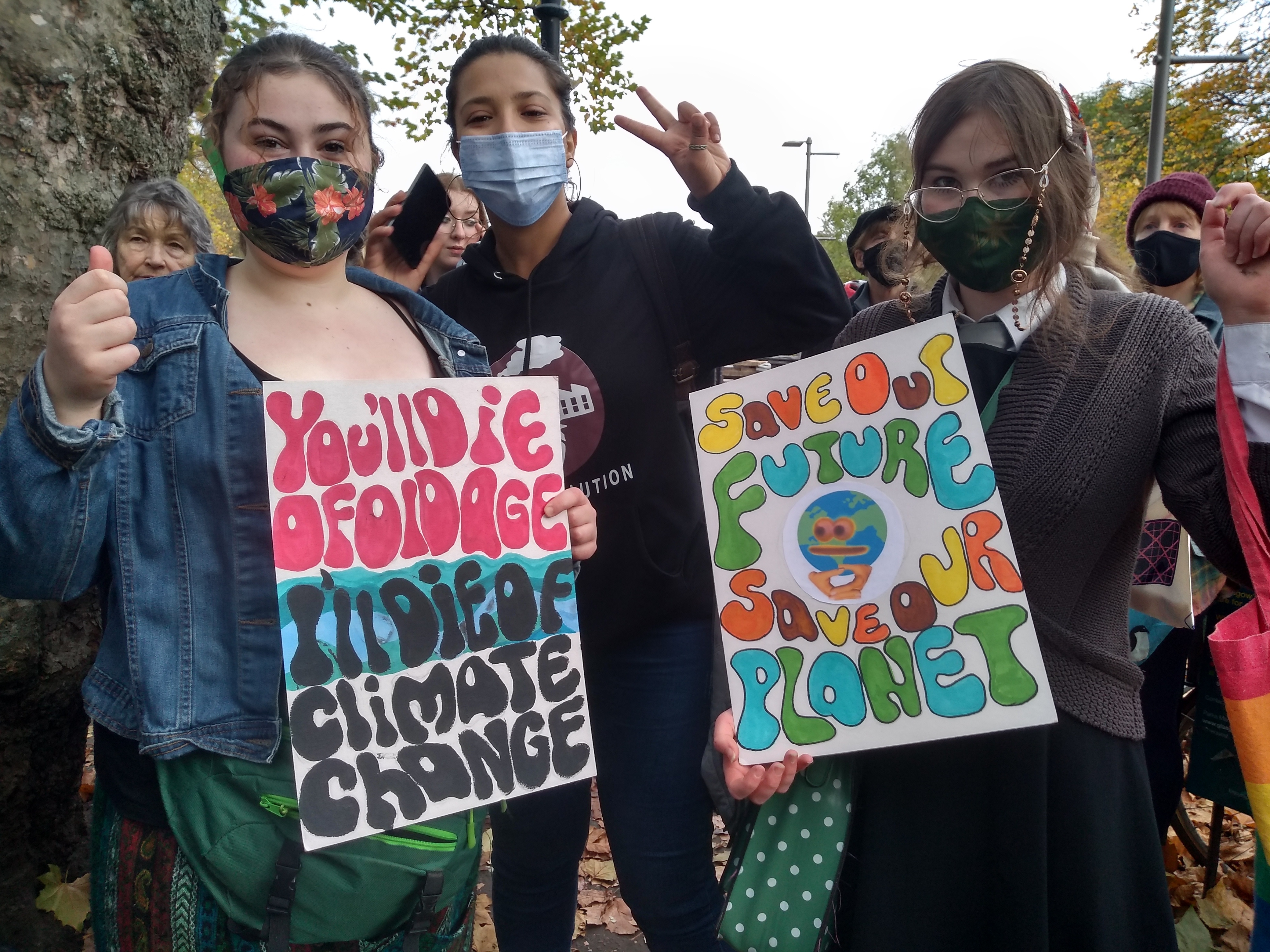 Three young people at COP26 protest, holding up signs about climate change