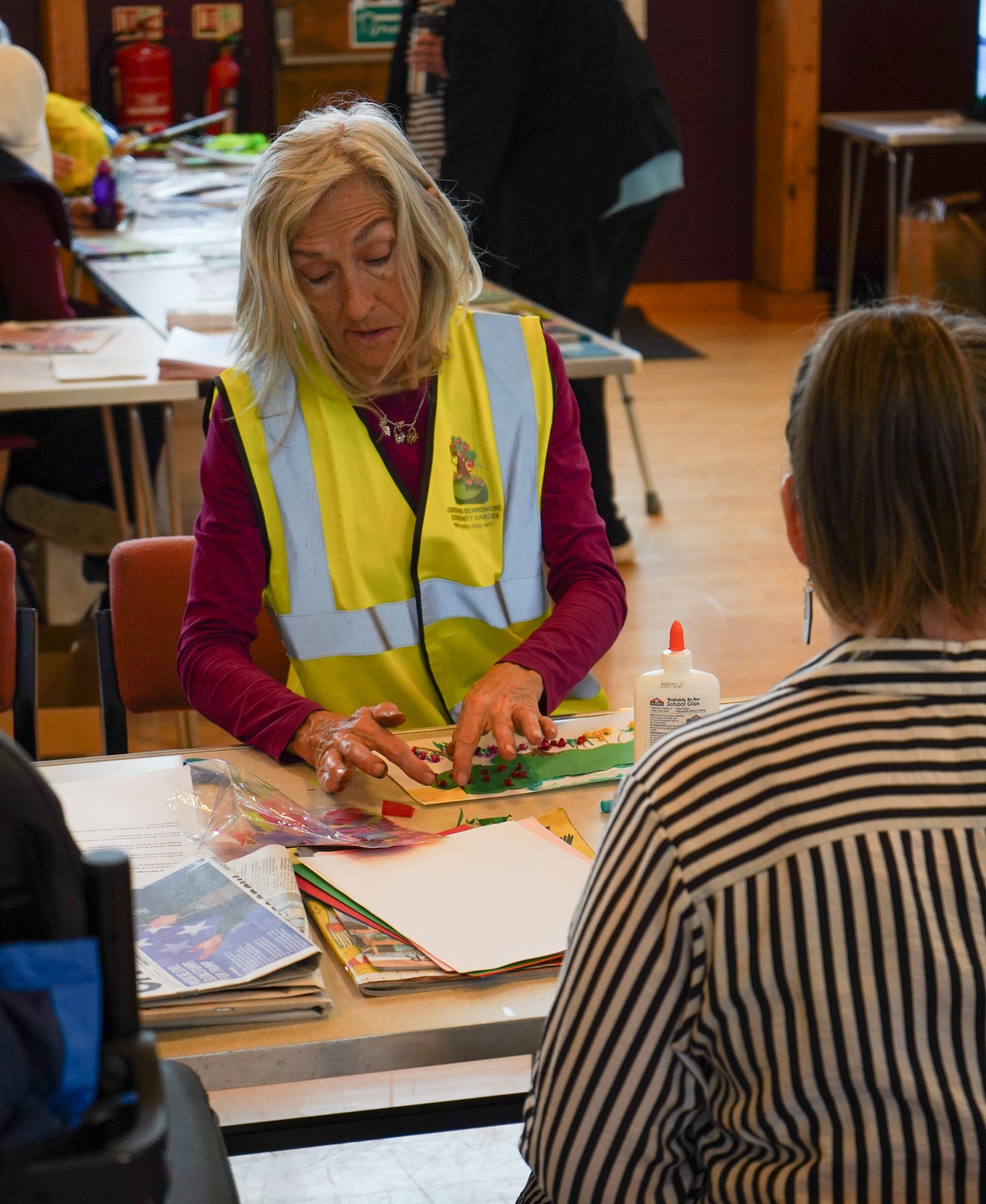 woman sitting at a table, wearing a high vis vest, creating some art work