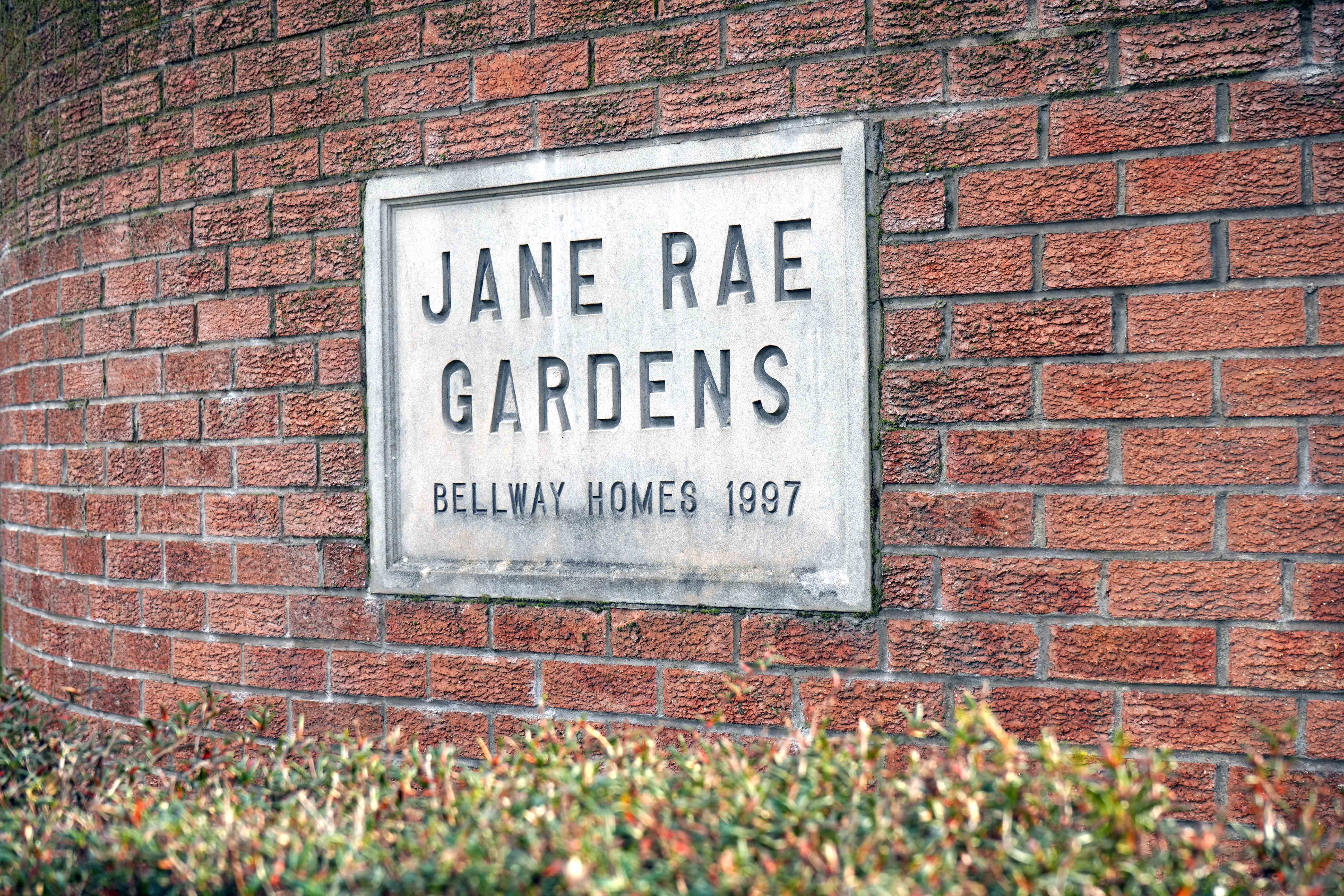 grey stone sign for Jane Rae gardens on a red brick wall