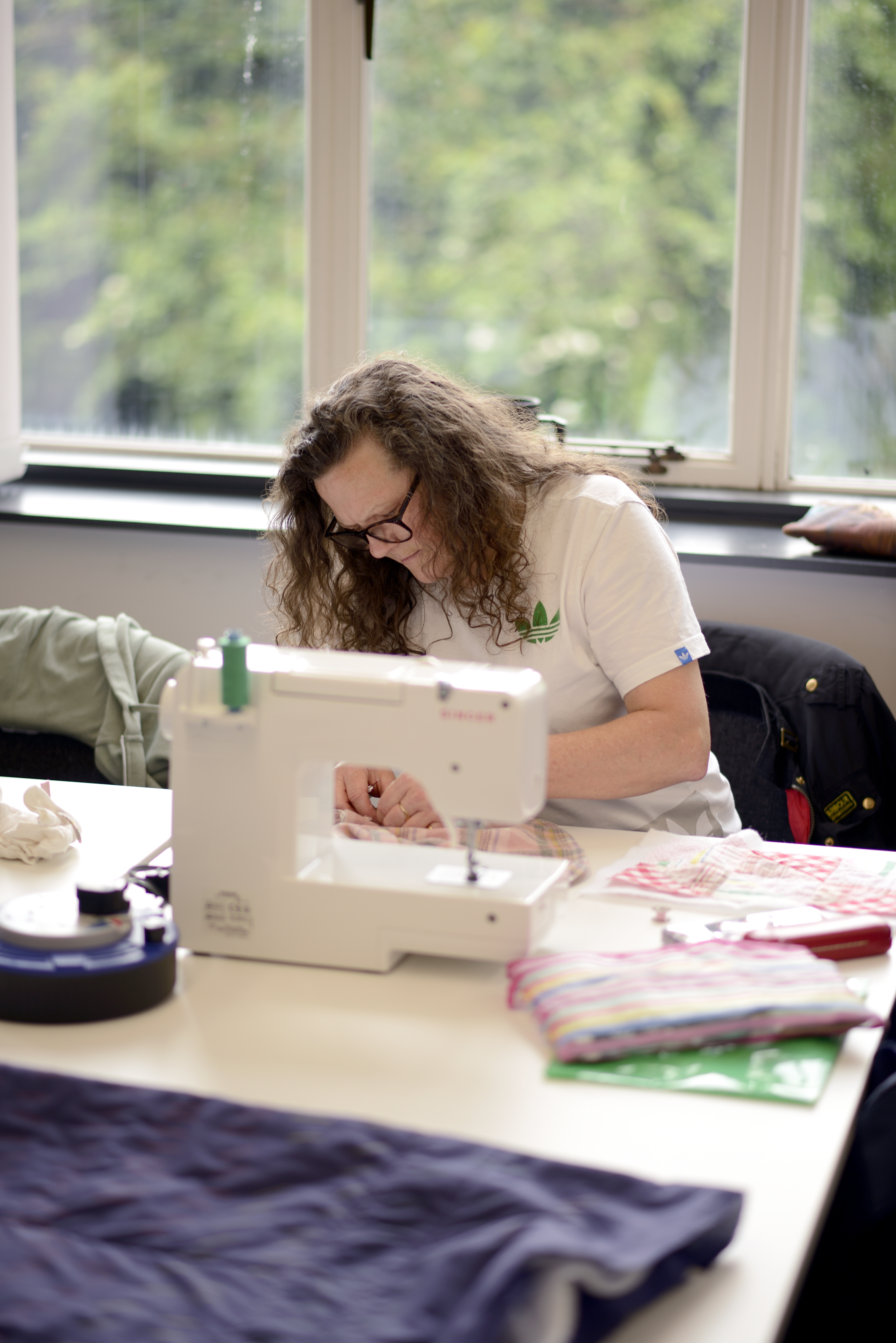 woman working at a table, with sewing machine on top of it.