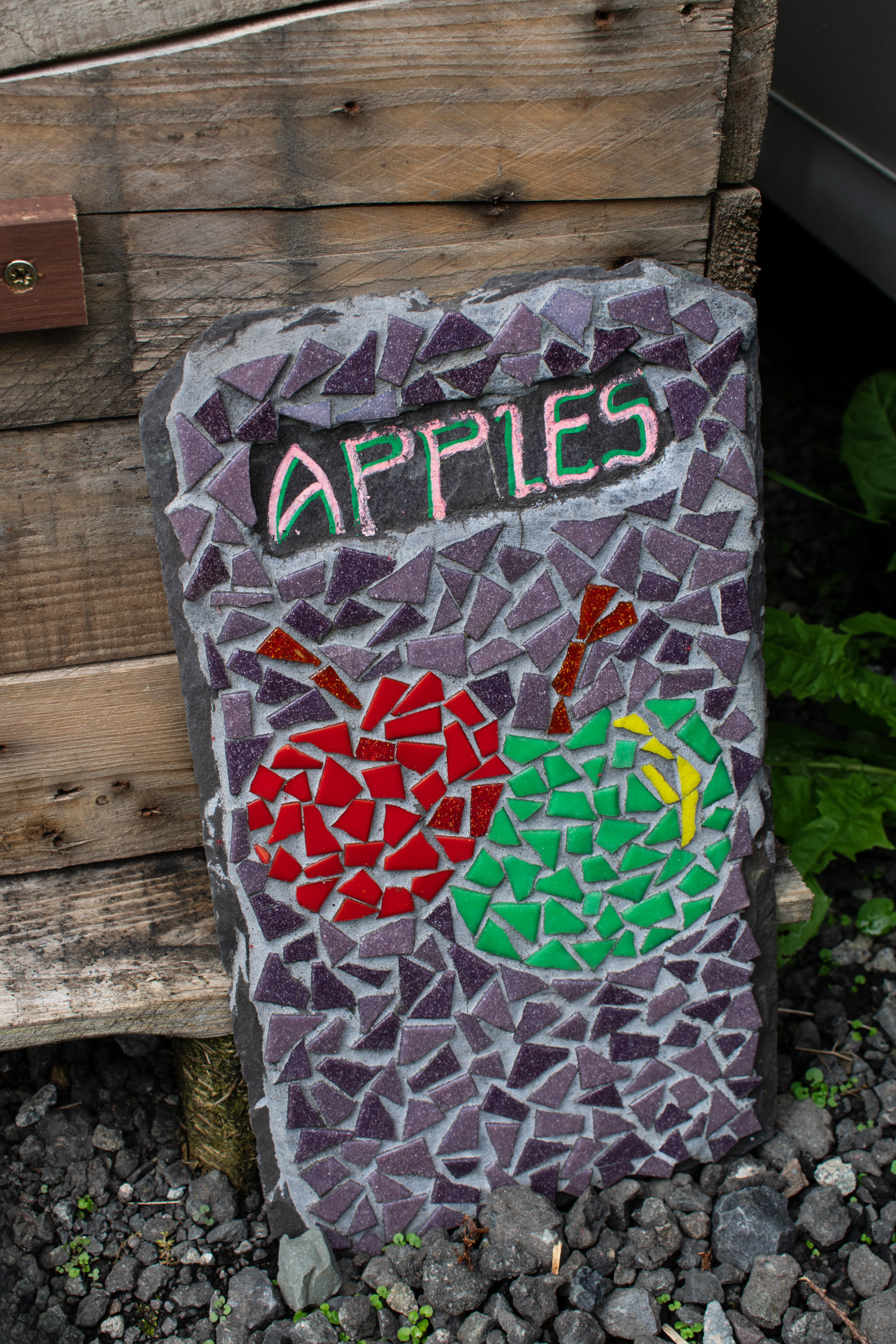 a sign made from broken pottery, saying 'apples'