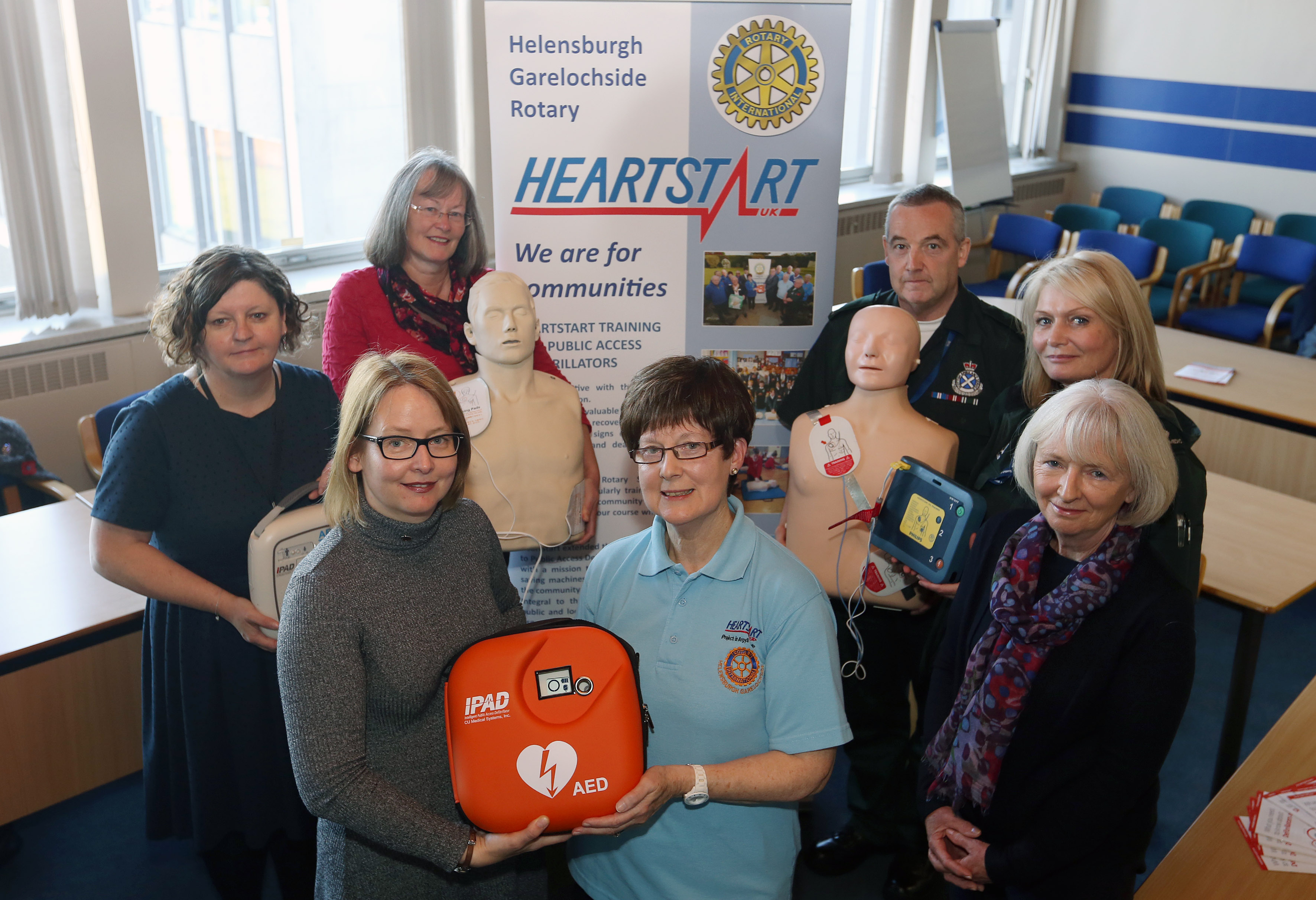 Group of people standing posing for a photograph. Two are holding a defibrillator and one holding a CPR dummy