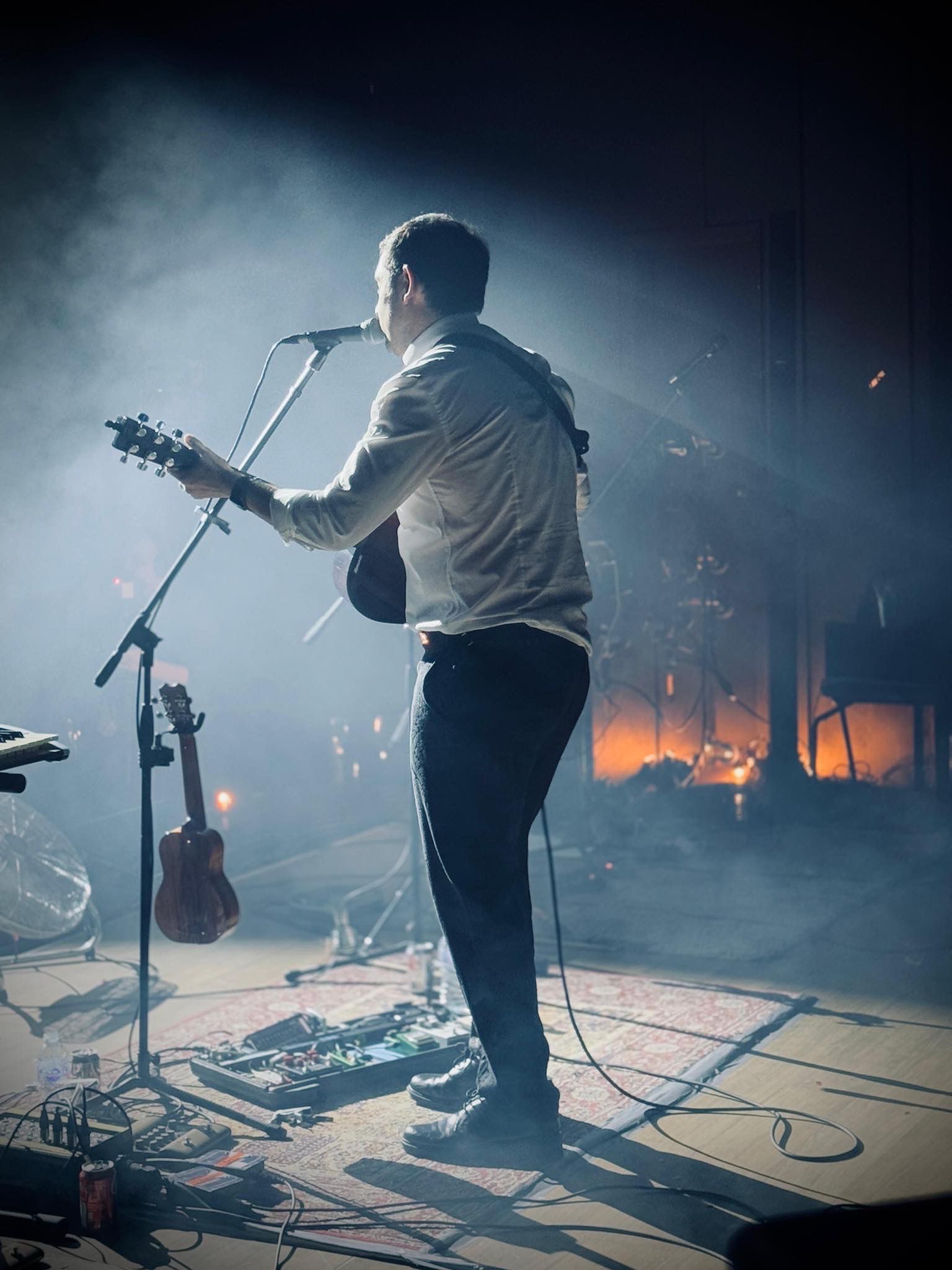 Crispin on stage, facing the audience,  playing his guitar and singing