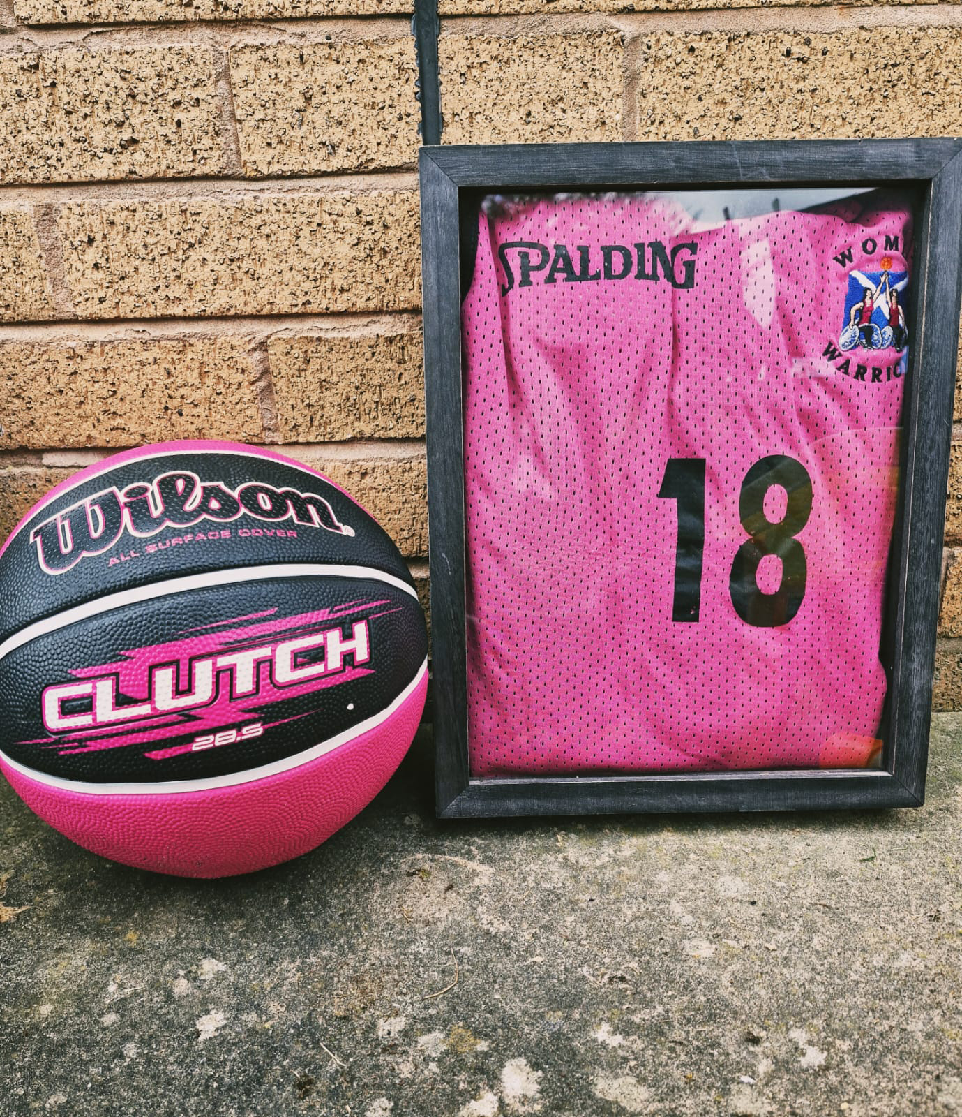 basketball uniform framed leaning against a wall next to a basket ball