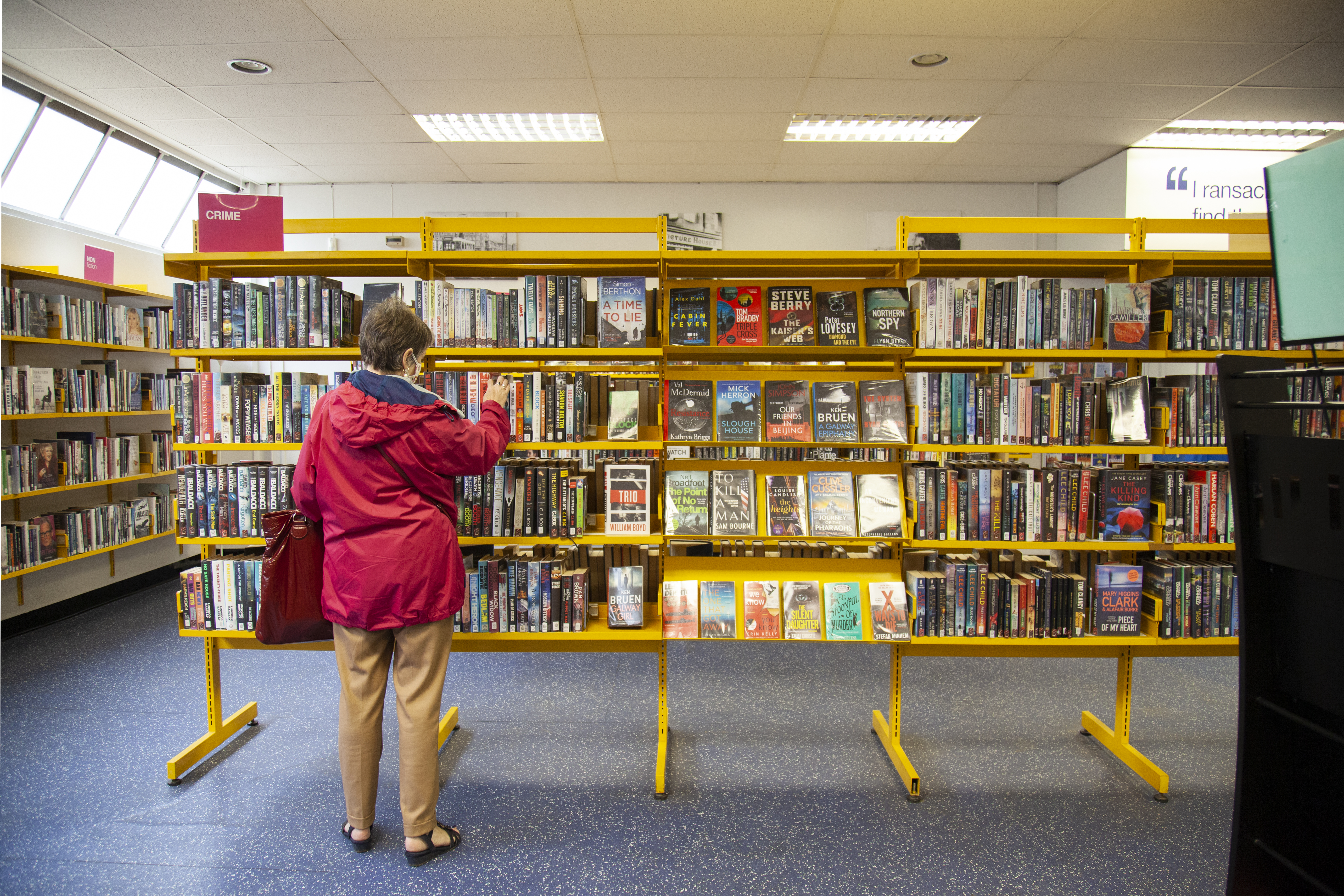 Woman is looking through the shelves of a library bookcase filled with books.
