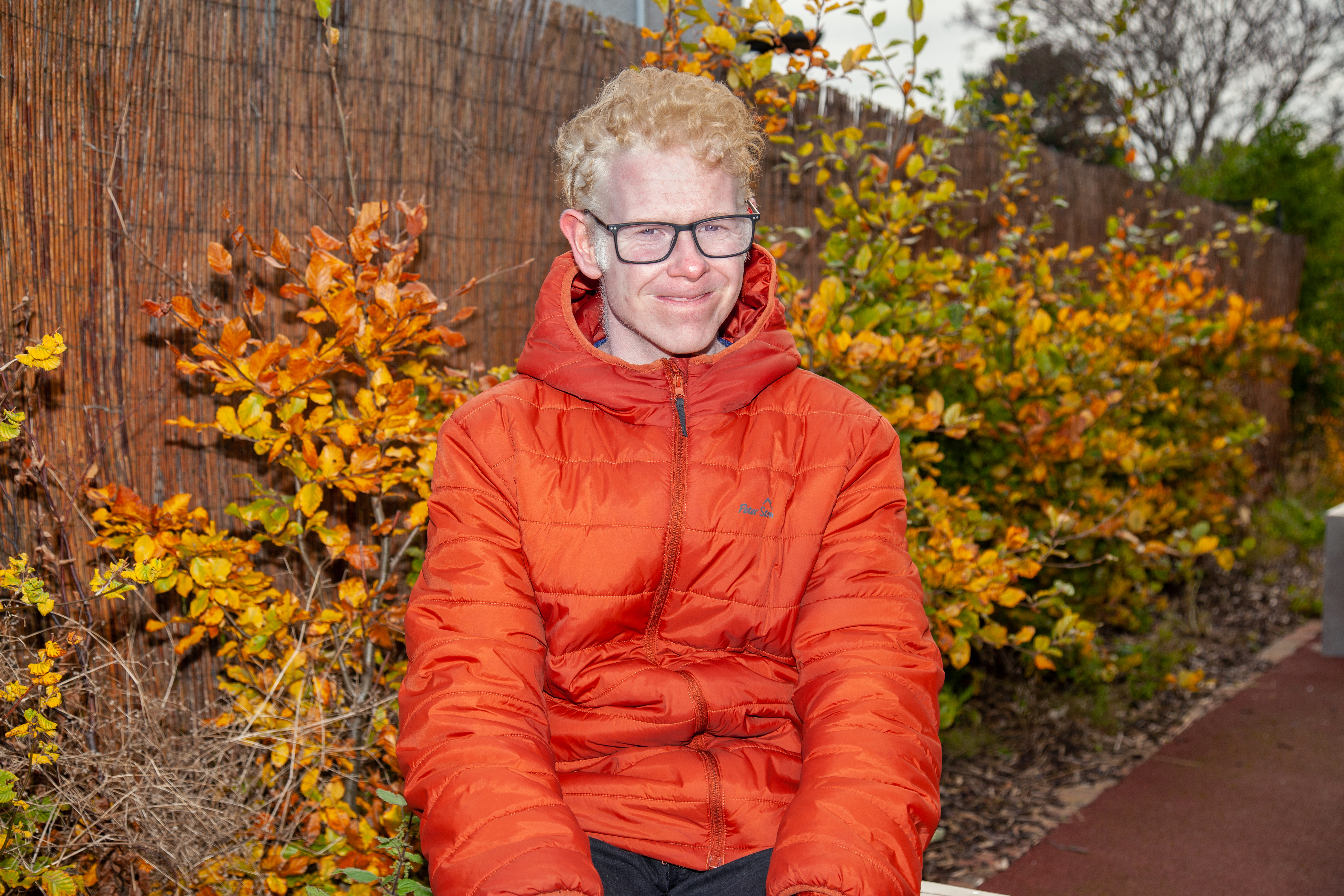 Mathew sitting outside with an orange jacket on