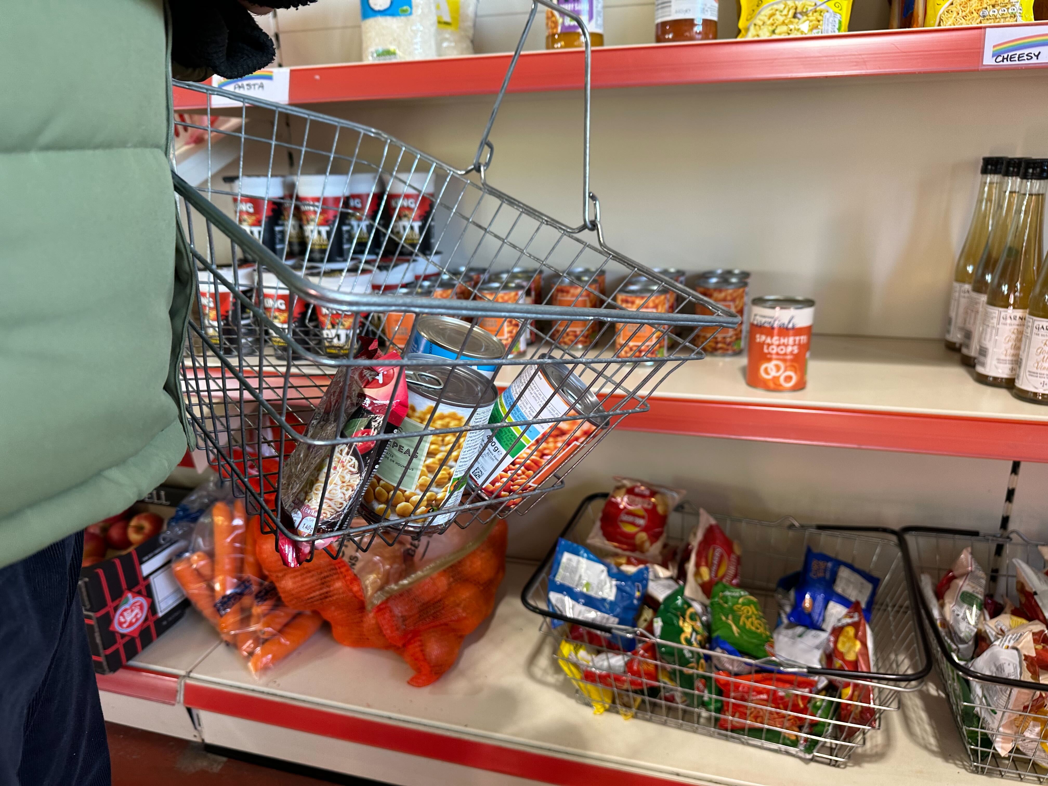 Shopping basket with tins and shelf in foodbank with various tinned items