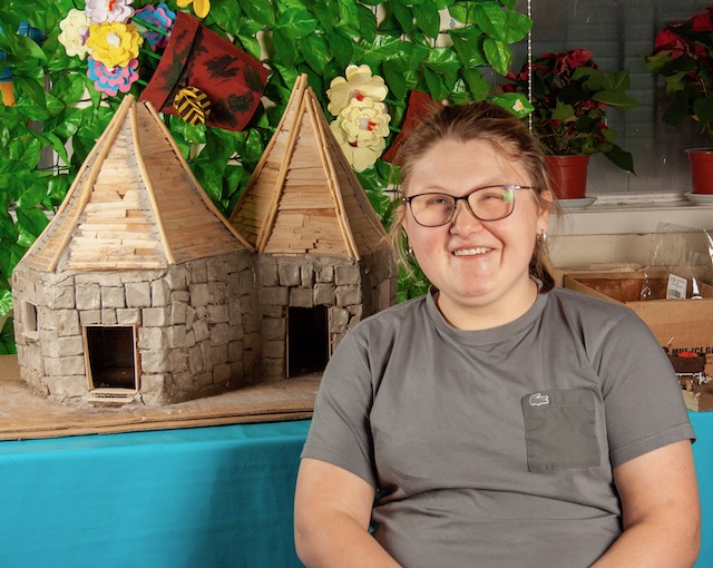Group member sitting in front of artwork created from rubbish