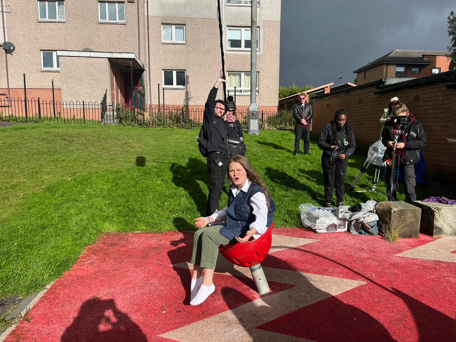 Film crew and actor filming on set in a children's play park