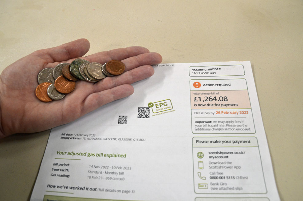 a hand holding small coins lying over an energy bill