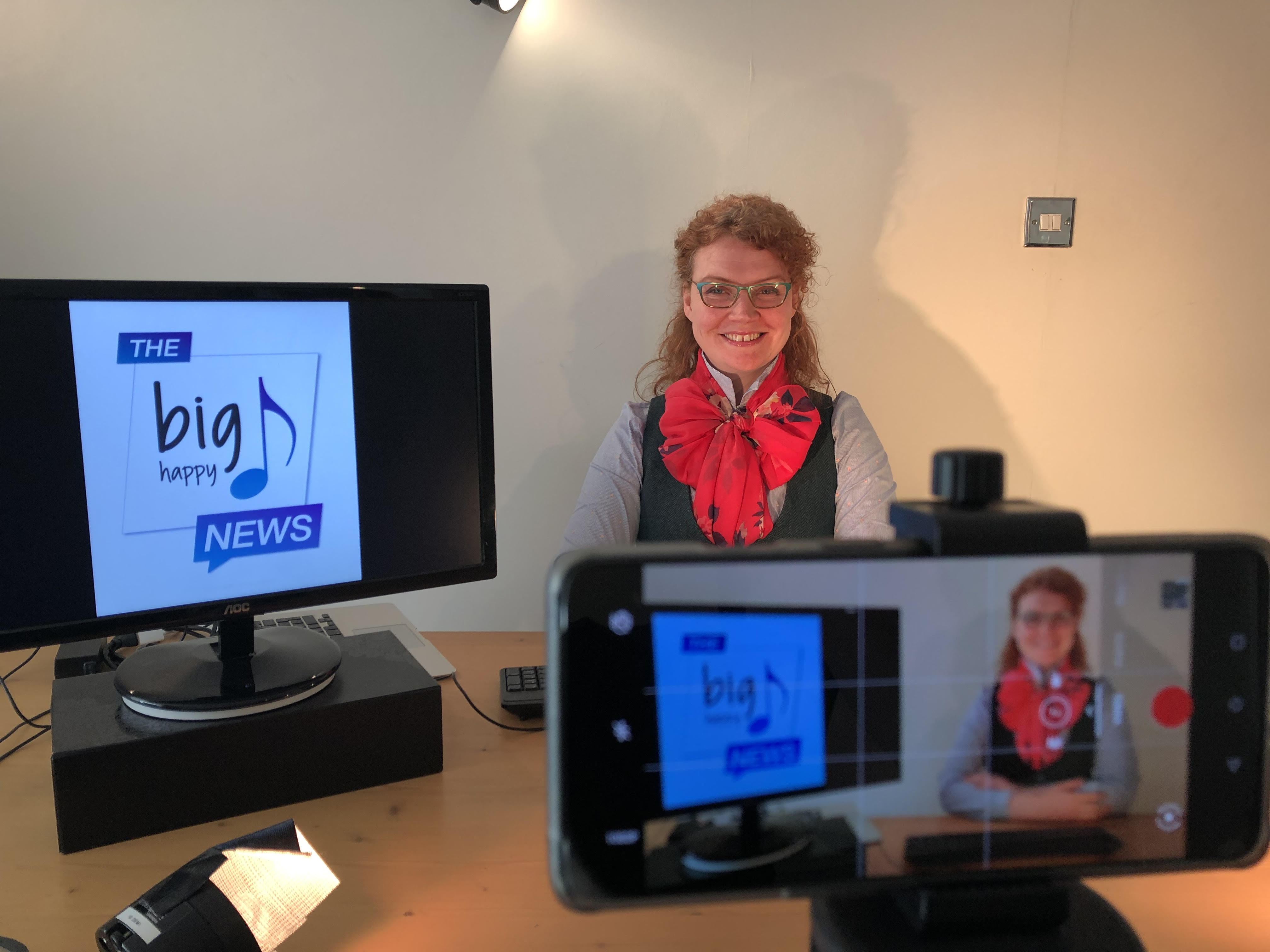 A woman presenting a slideshow with the slides on a monitor to her right, a mobile phone is in the foreground also recording her.