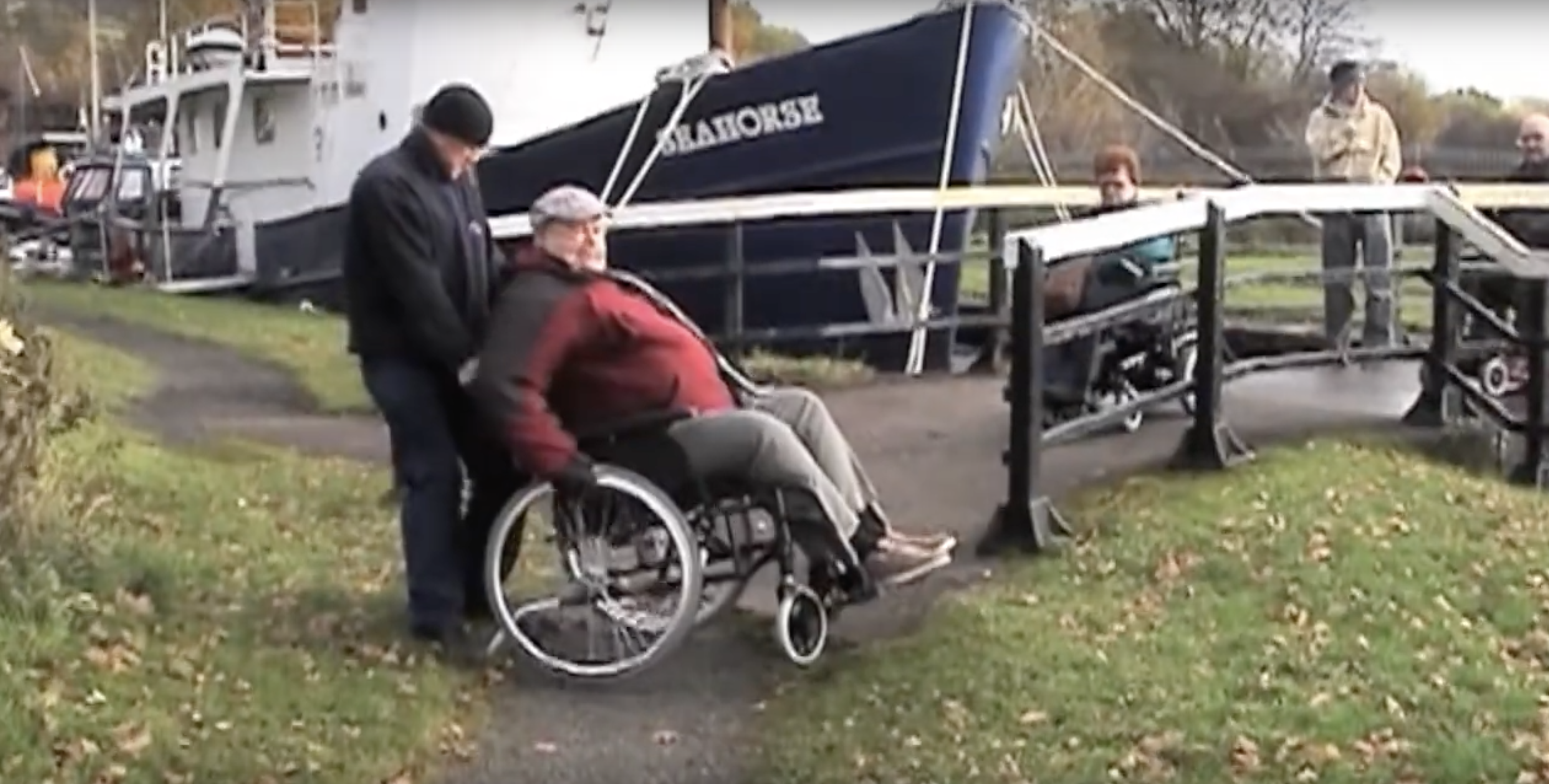 man being pushed in wheelchair across bridge