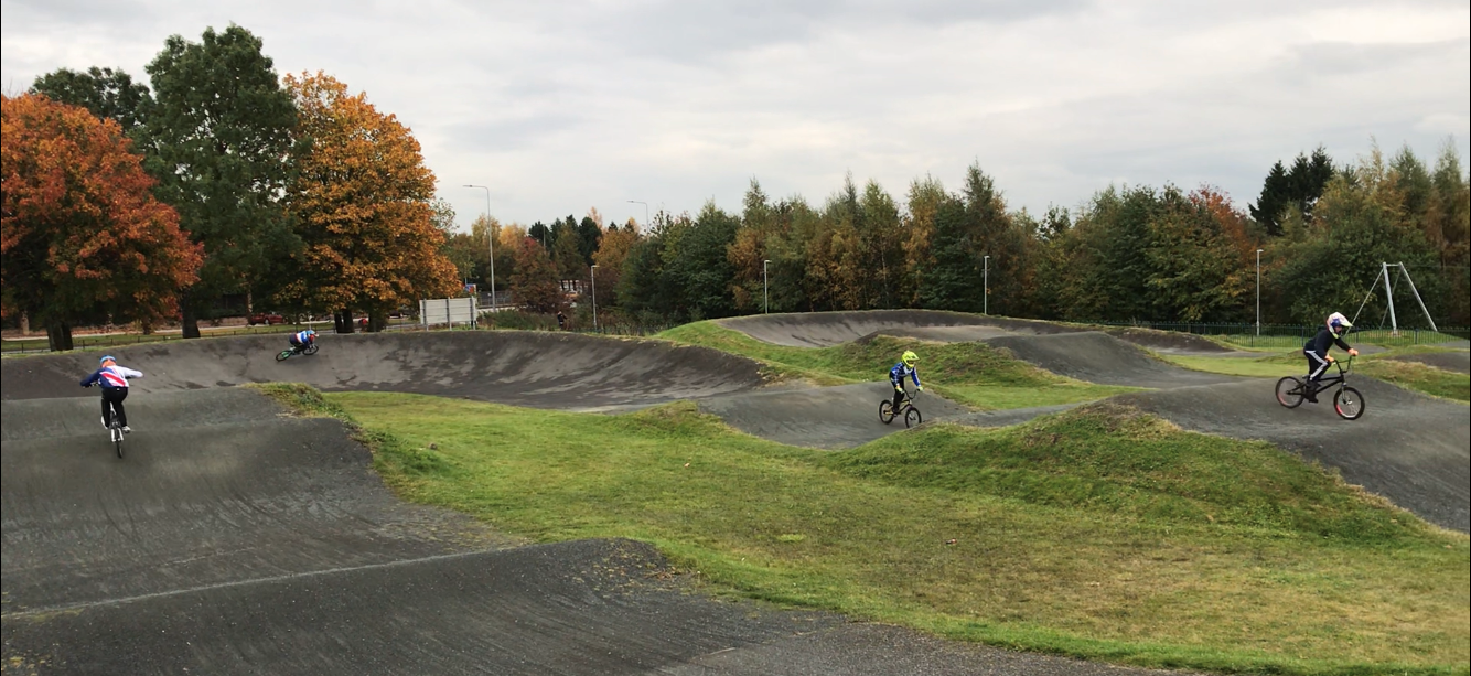 Landscape image of BMX track with a few small racers dotted around it.