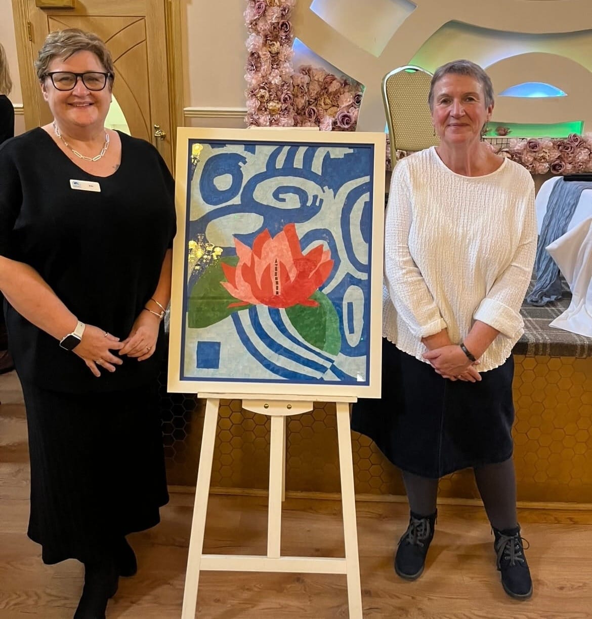 Two women standing next to a canvas of the book front cover artwork