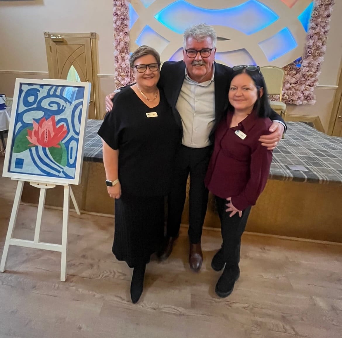 Three people, two women and one man, standing in front of a stage smiling.