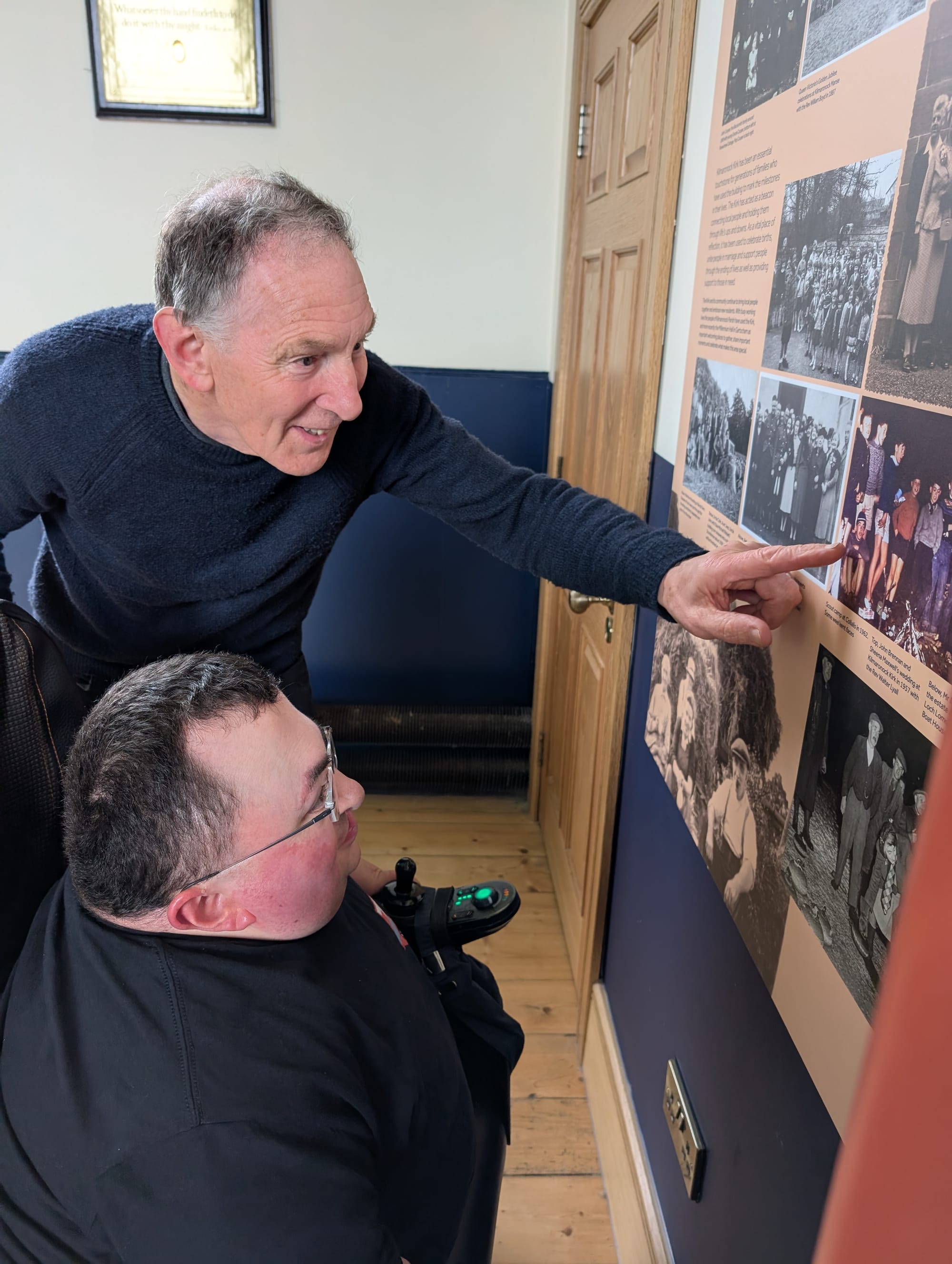 Picture of Hugh pointing at a photo on the display on the wall and Steven looking at it