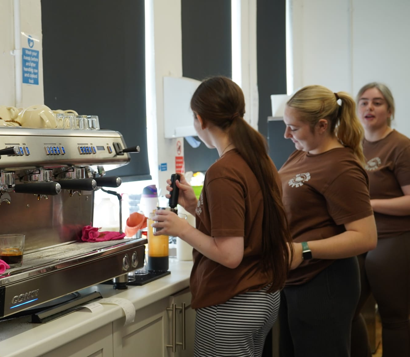 Three young women, standing at a worktop, side on to the camera, mixing drinks 
